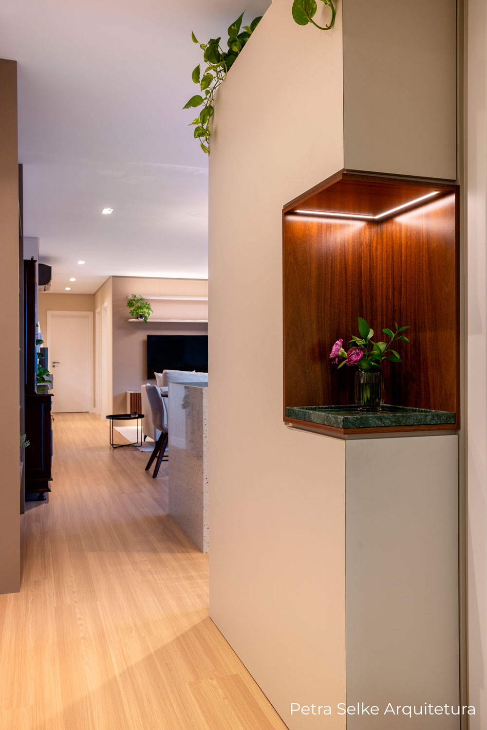 Hall de entrada moderna e minimalista com painel usinado em MDF bege, nicho em MDF madeirado escuro e bandeja em mármore Verde Alpi. Porta discreta na frente