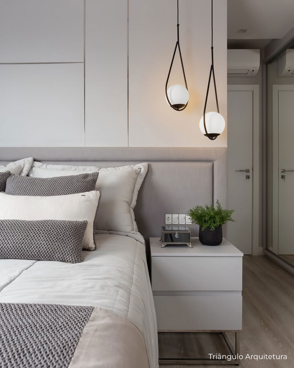 Quarto moderno e clean, painel em MDF branco com detalhes em perfil metálico prata, cabeceira estofada cinza, com móvel de canto em cinza e pé em ferro cromado
